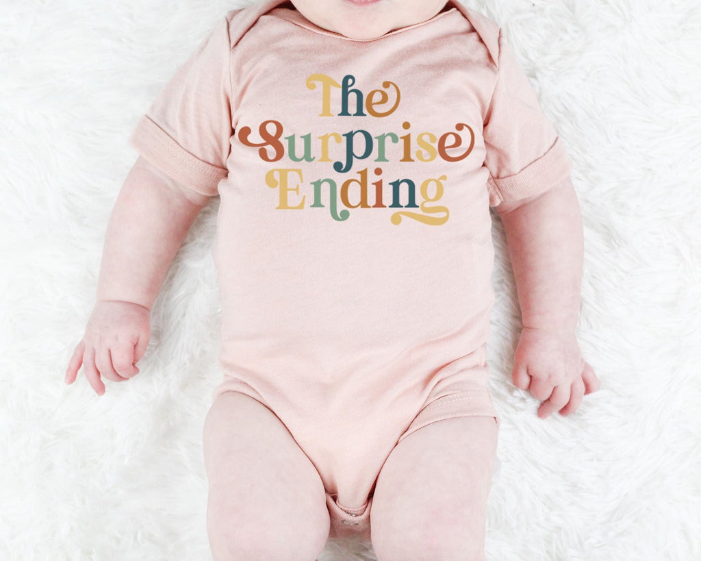 a baby wearing a pink bodysuit that says the surprise ending