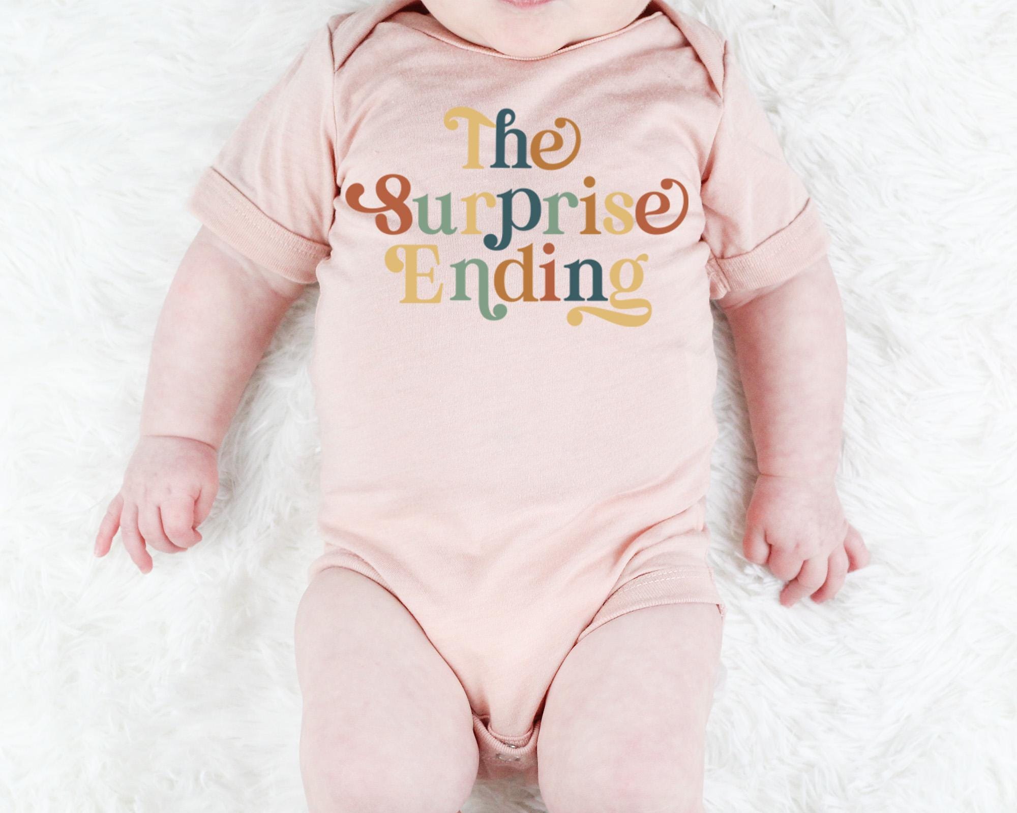 a baby wearing a pink bodysuit that says the surprise ending