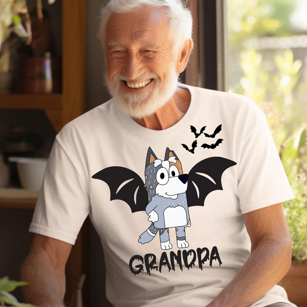 A smiling older man wearing a white t-shirt with a cartoon image of a dog with bat wings and the word "GRANDPA" printed on it.