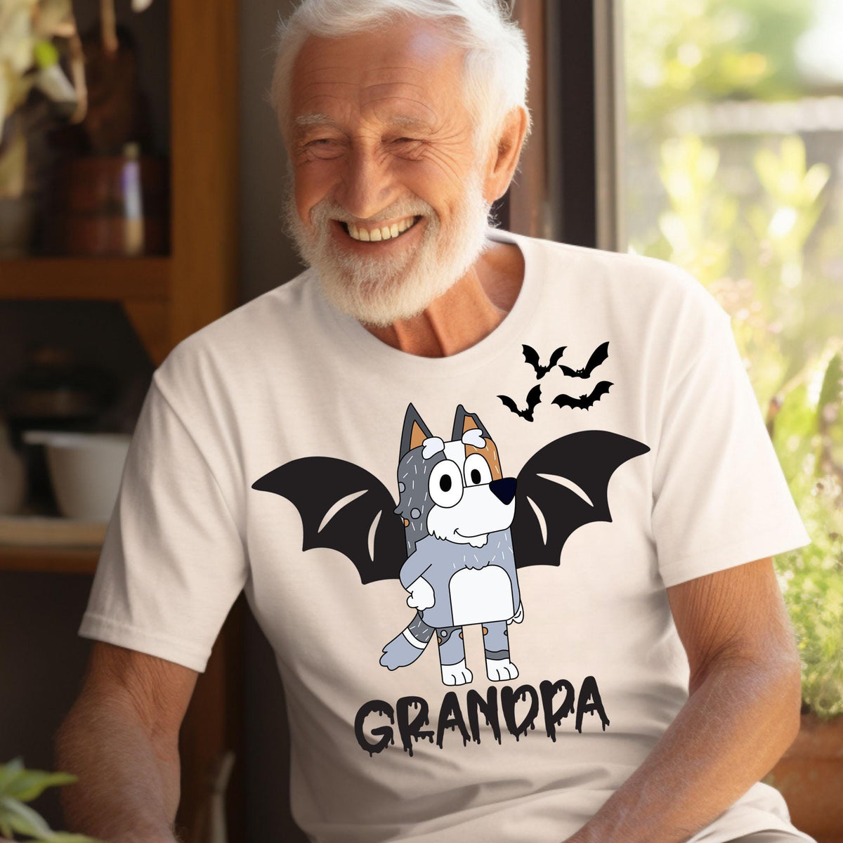 A smiling older man wearing a white t-shirt with a cartoon image of a dog with bat wings and the word "GRANDPA" printed on it.