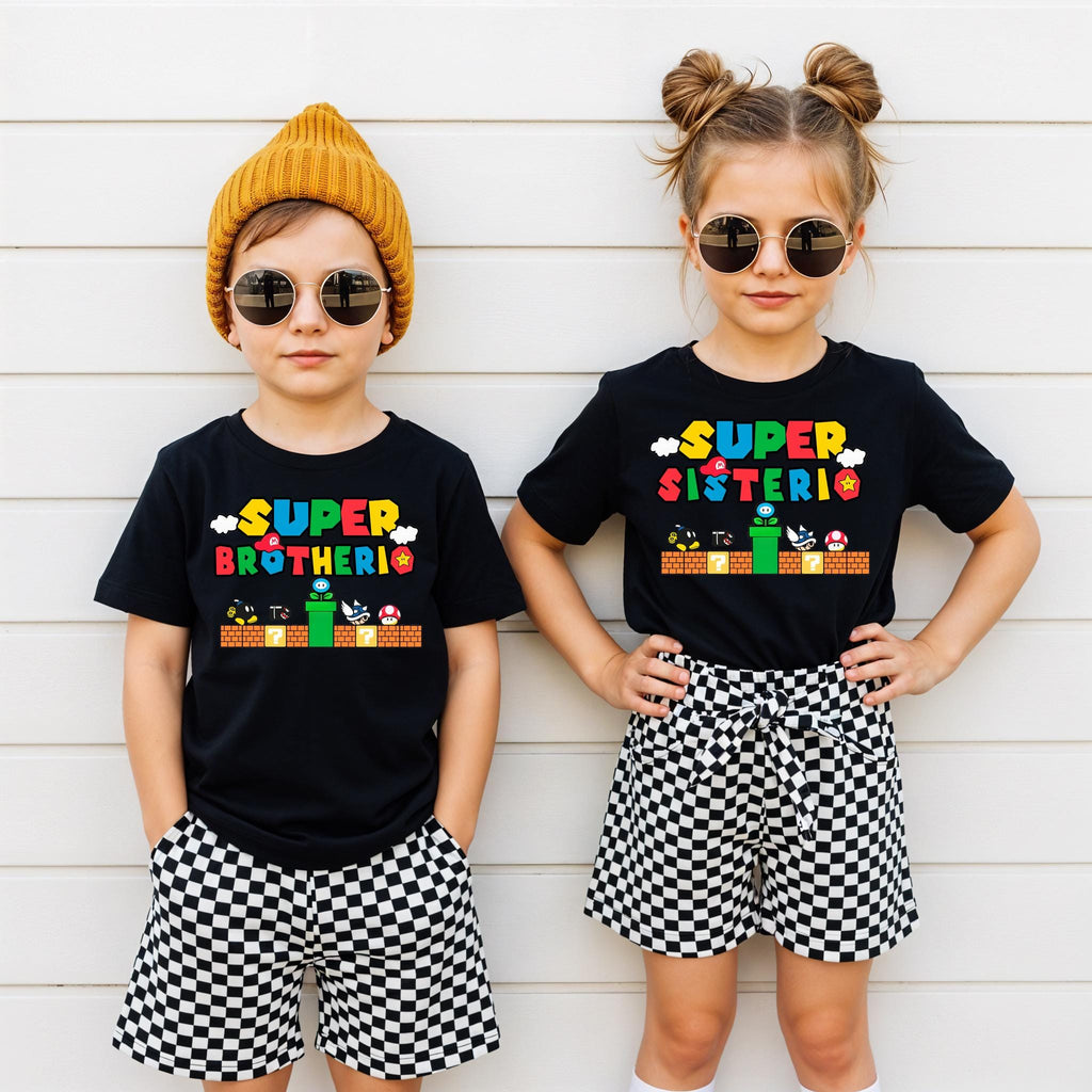 Two children wearing black t-shirts with a colorful design and sunglasses, standing against a white wall.
