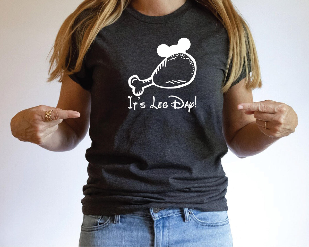 A woman wearing a black t-shirt with a white graphic and text, pointing at the shirt with her fingers.