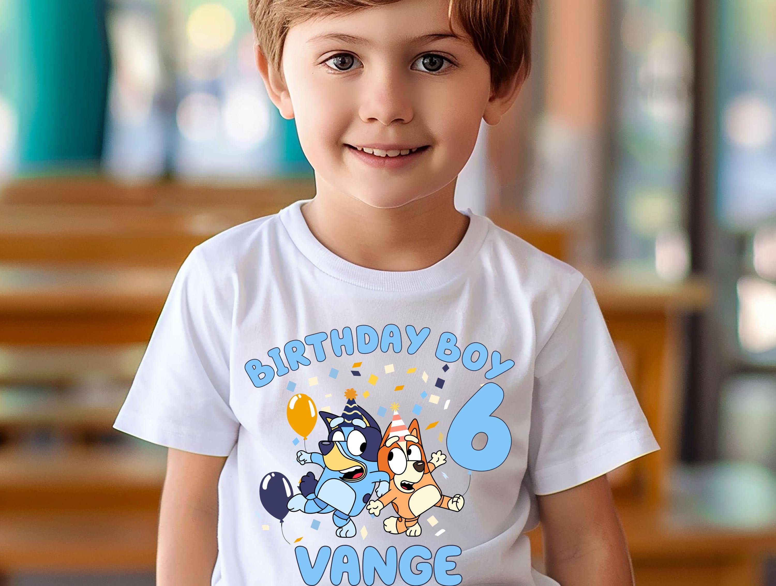 A young boy wearing a white t-shirt with a birthday theme and cartoon characters.