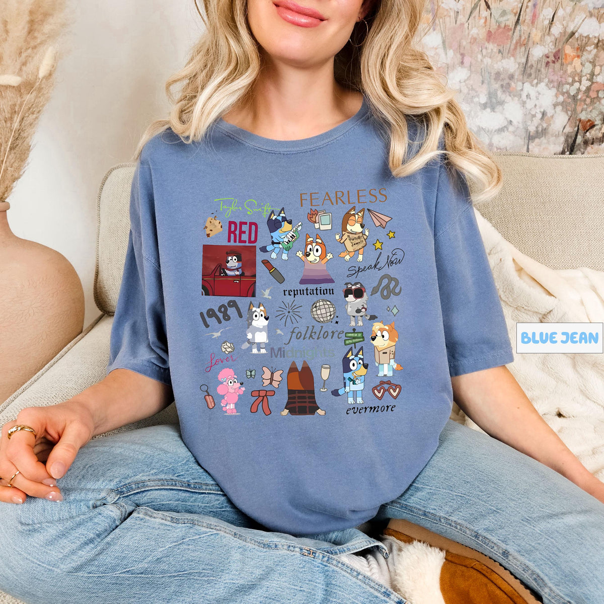 A woman wearing a blue t-shirt with various cartoon characters and text printed on it, sitting on a couch.