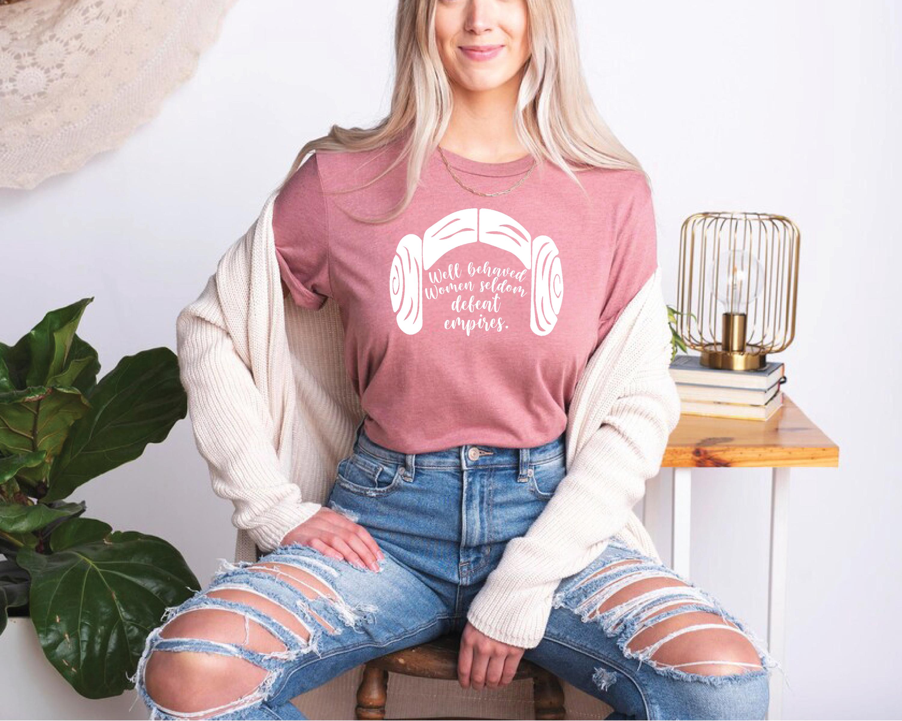 a woman sitting on a stool wearing a pink shirt and ripped jeans