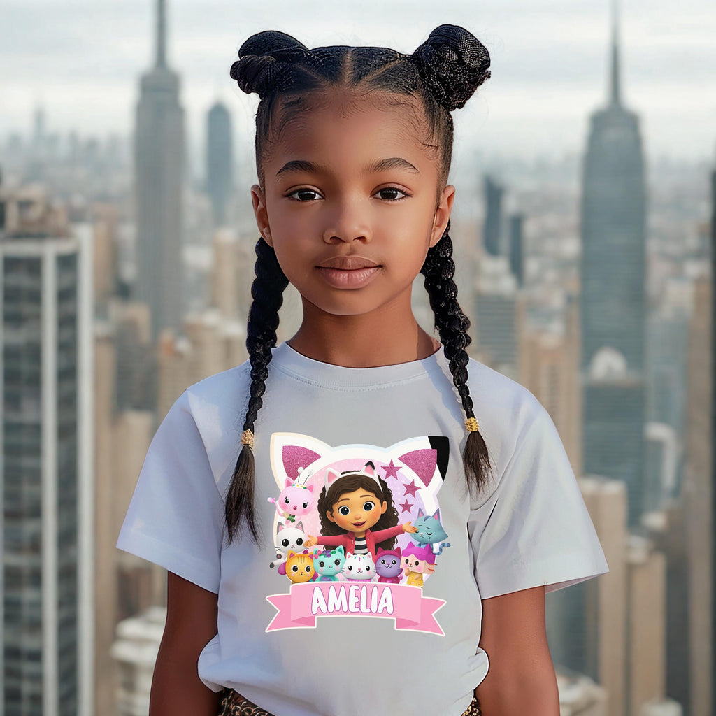 A young girl with braided hair wearing a white t-shirt with a cartoon character and the name "Amelia" printed on it, standing in front of a city skyline.