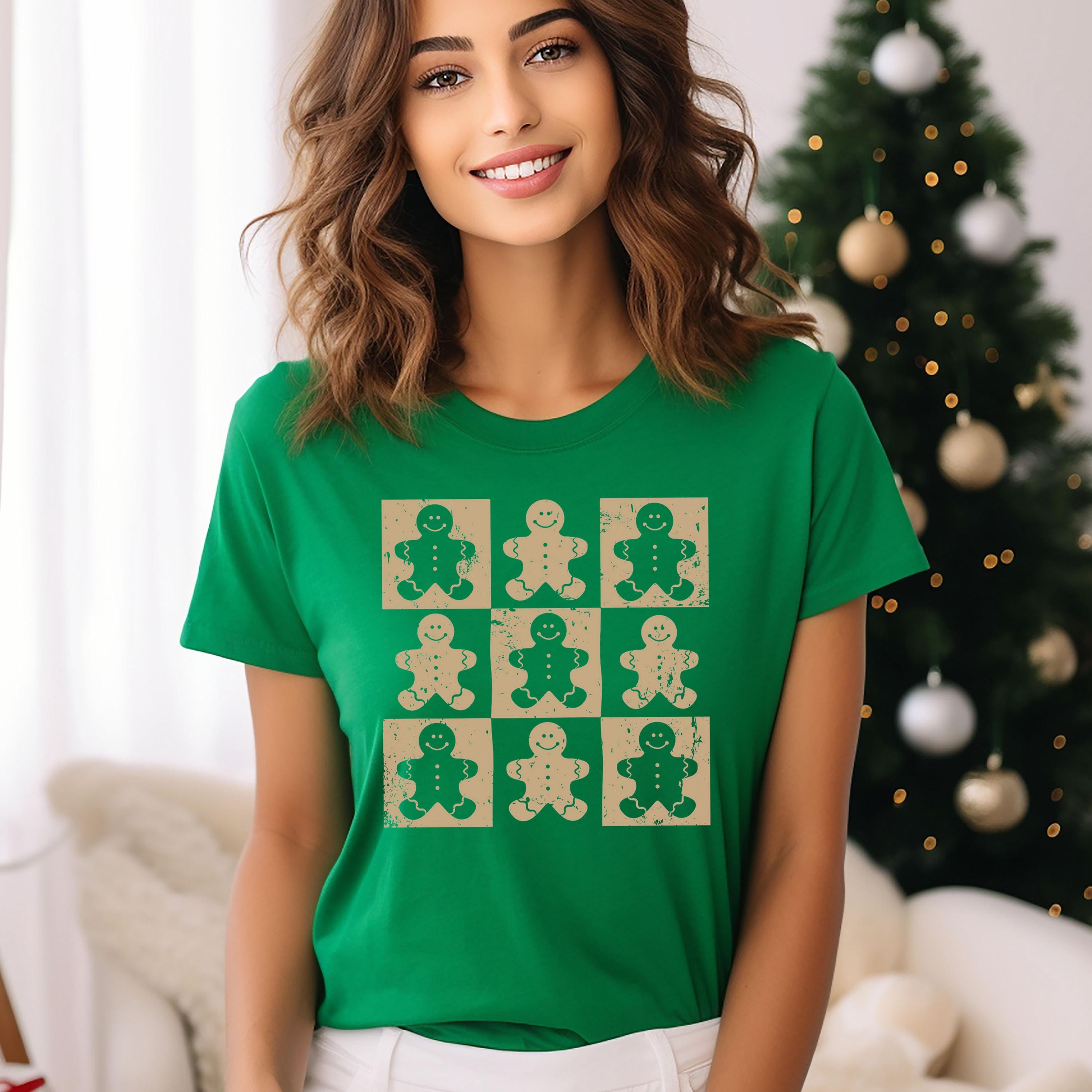 A woman wearing a green t-shirt with a graphic of nine smiling gingerbread man figures.