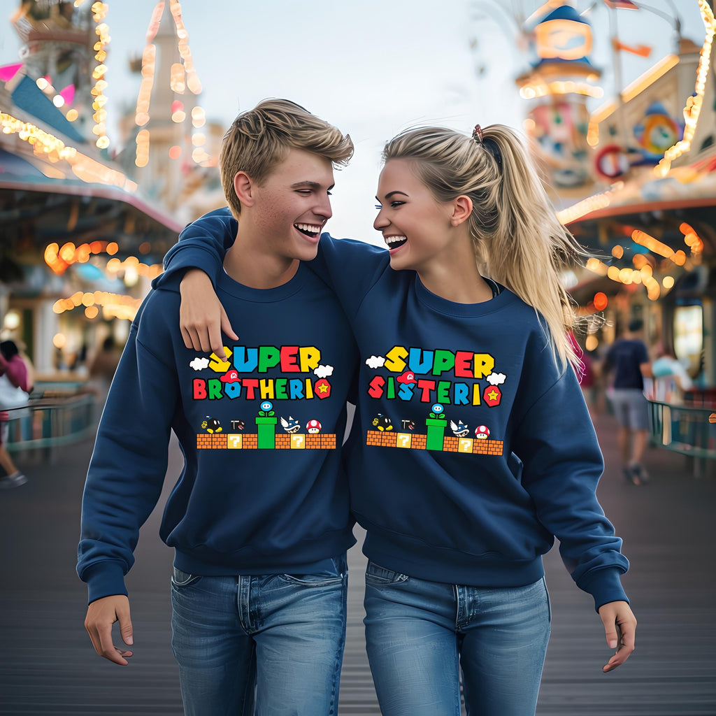 A young man and woman are standing close together, smiling and embracing each other, wearing matching blue sweatshirts with a colorful design.