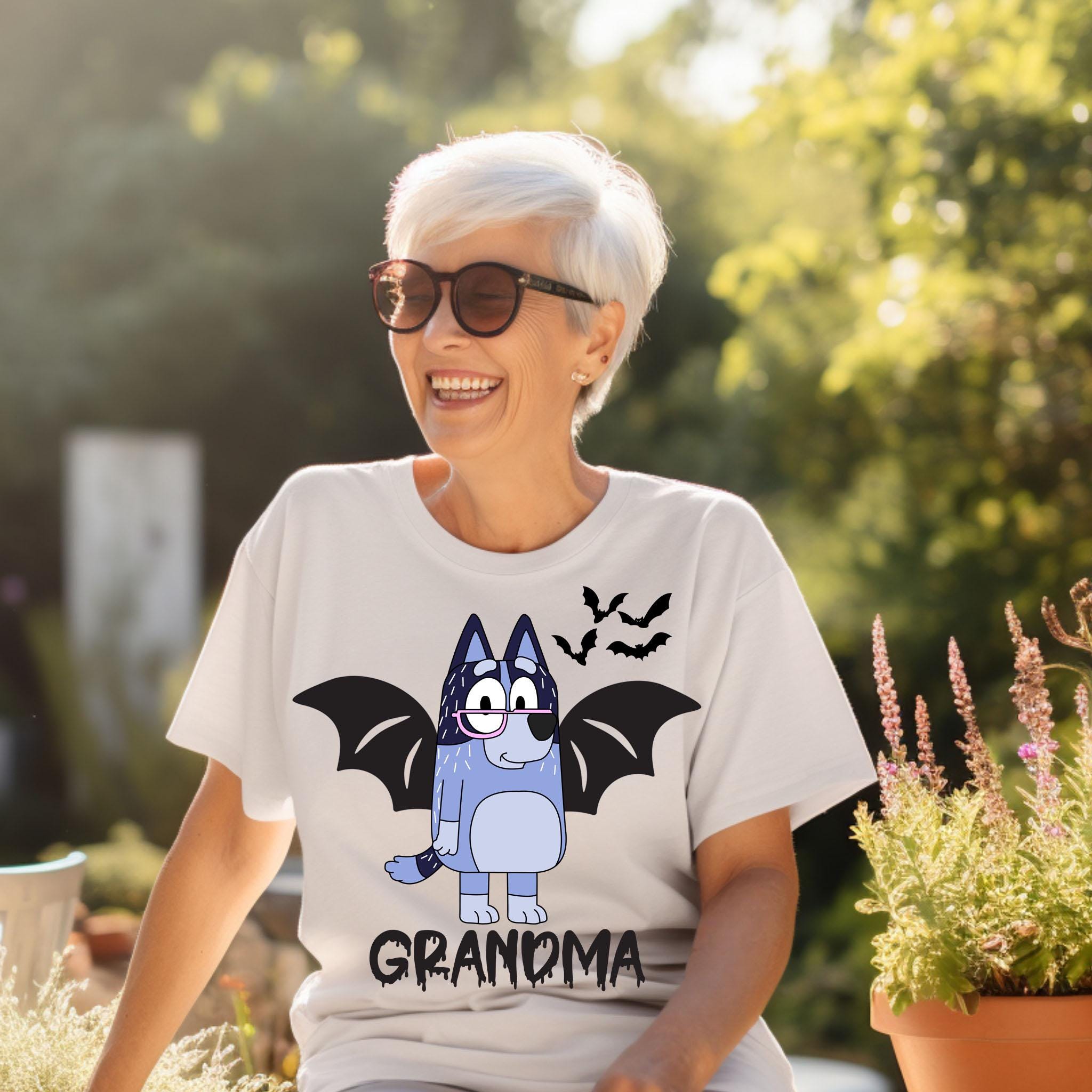 A smiling older woman wearing a white t-shirt with a graphic of a bat-like character and the word "GRANDMA" printed on it.