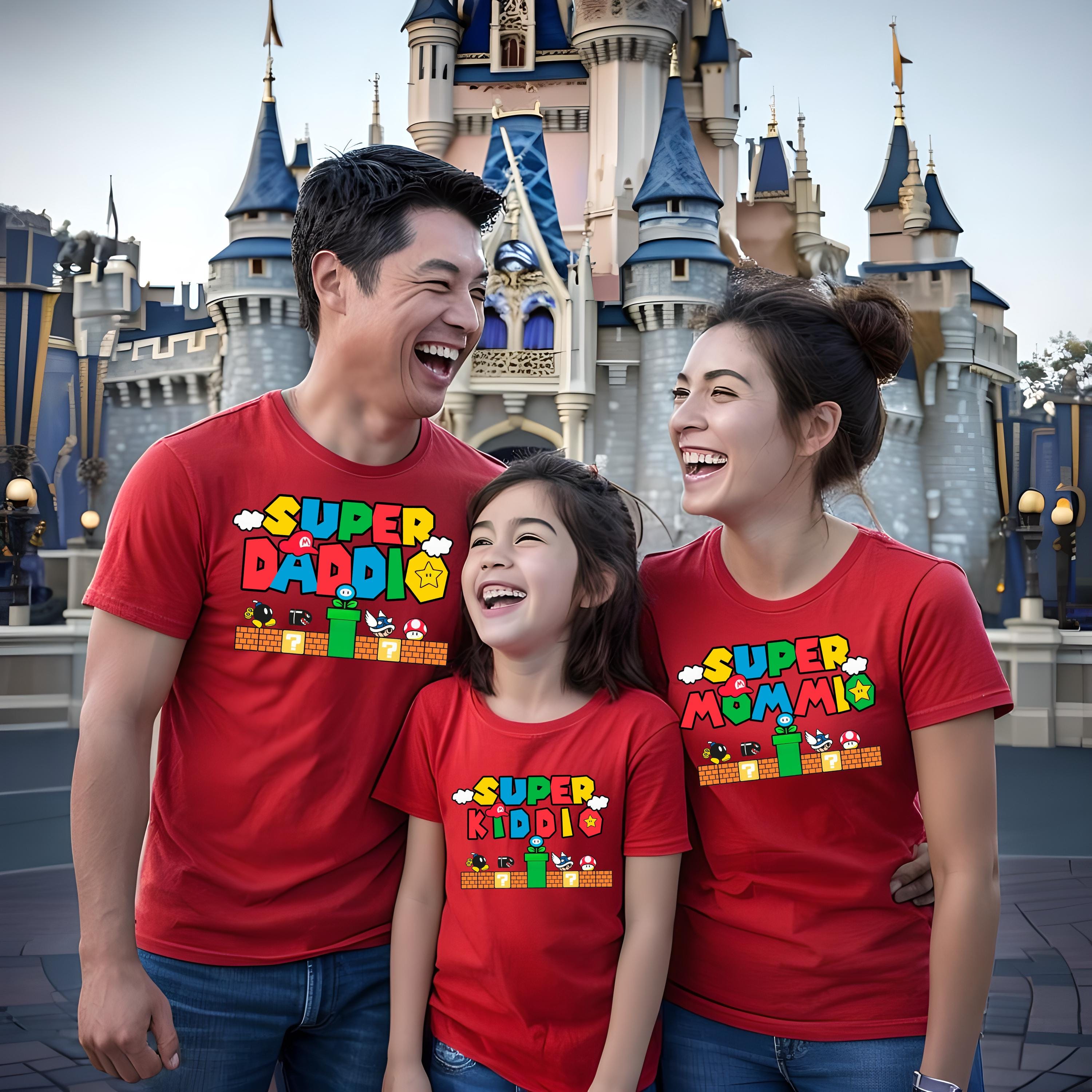 A man, a woman, and a child are all wearing red t-shirts with the text "SUPER KIDO" printed on them, smiling and posing in front of a castle.