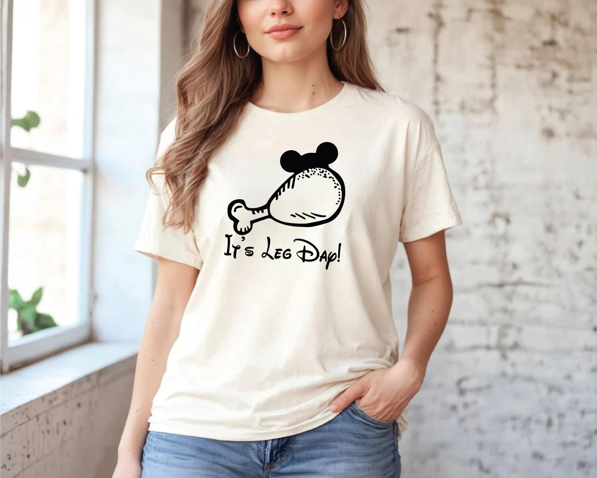 A woman wearing a white t-shirt with a graphic of a chicken and the text "It's leg dap!" printed on it.