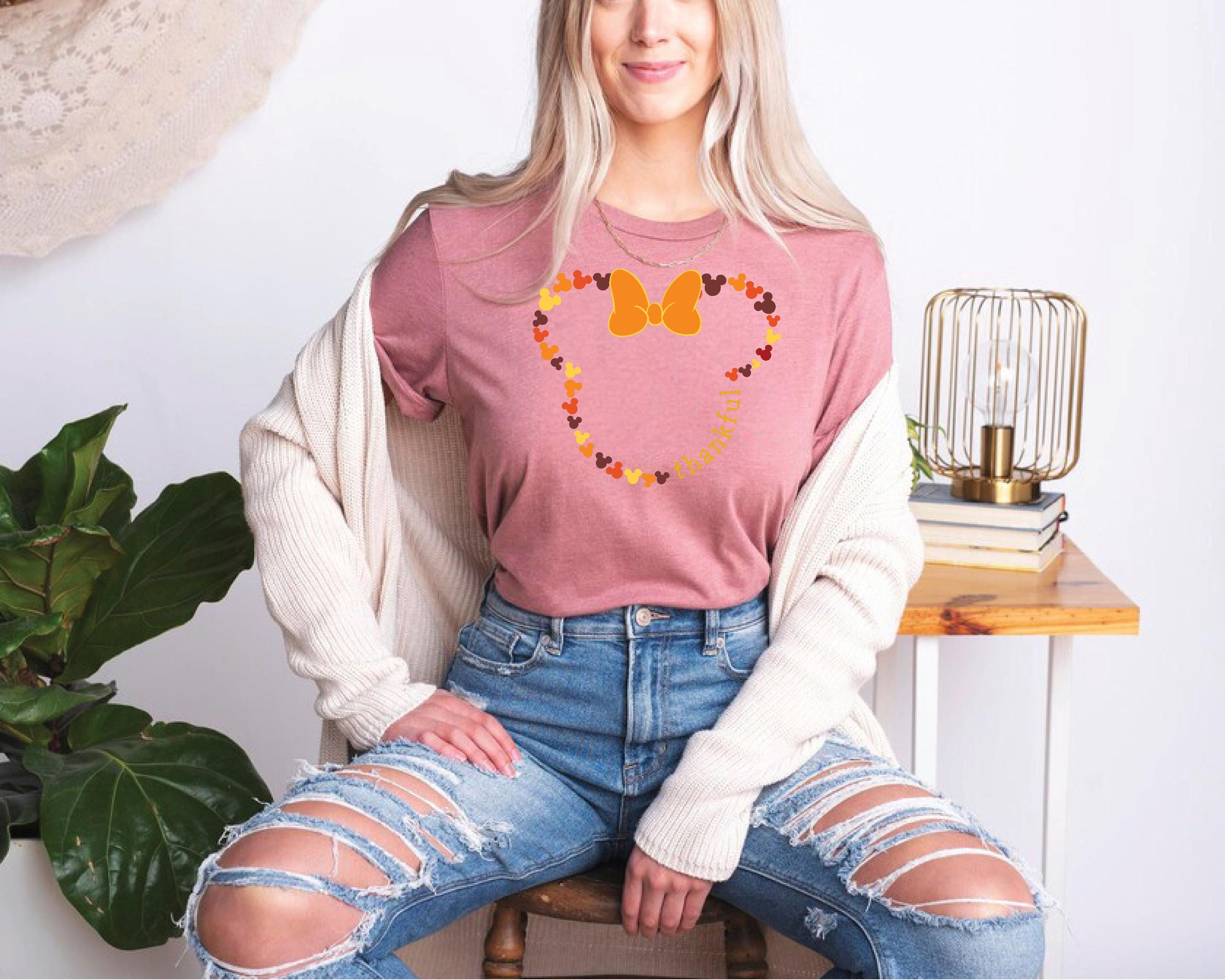 a woman sitting on a stool wearing a pink shirt and ripped jeans