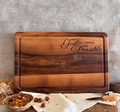 A wooden cutting board with the text "With all things are possible" engraved on it, along with a basket of nuts and a knife on a woven placemat.