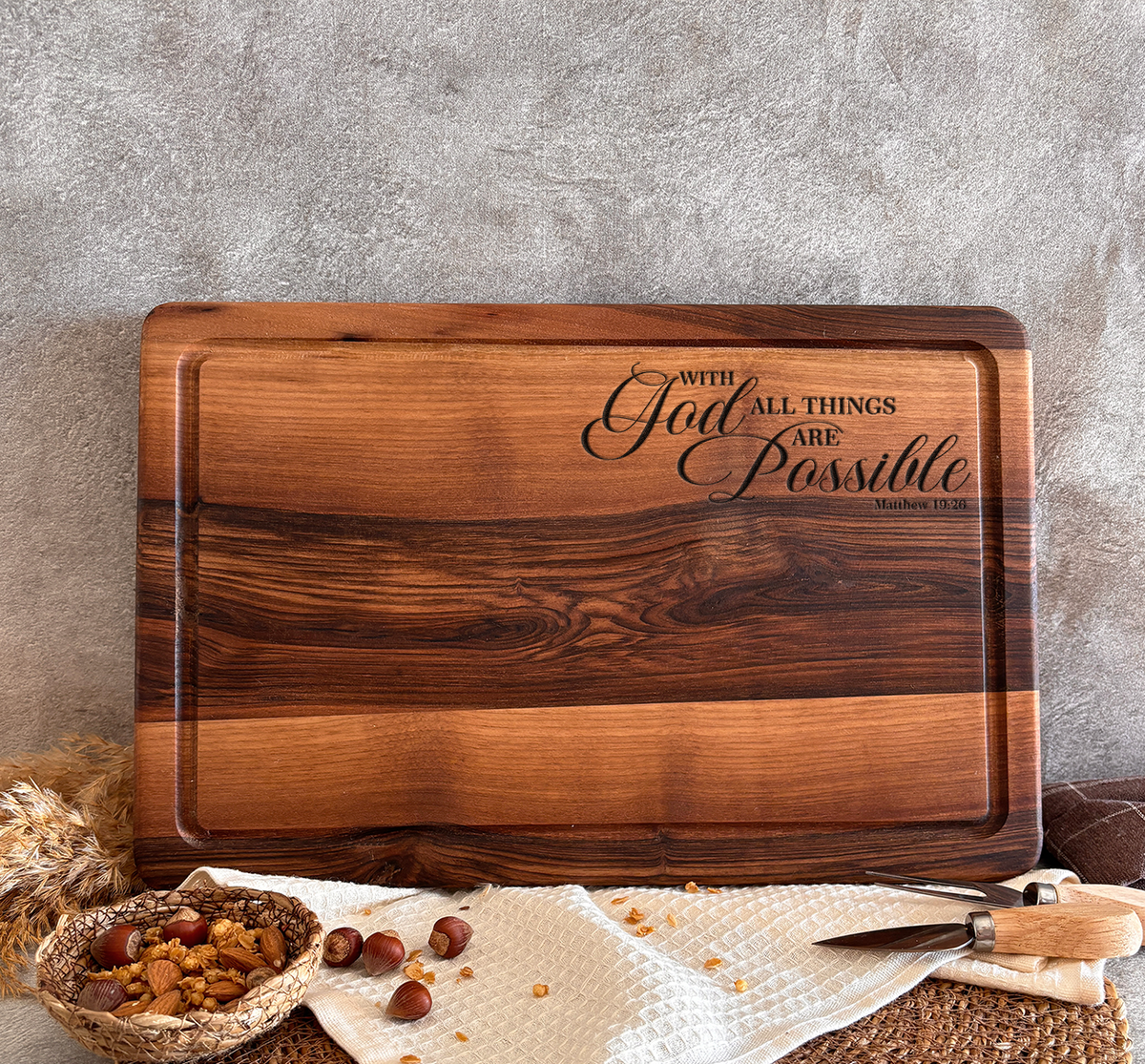 A wooden cutting board with the text "With all things are possible" engraved on it, along with a basket of nuts and a knife on a woven placemat.