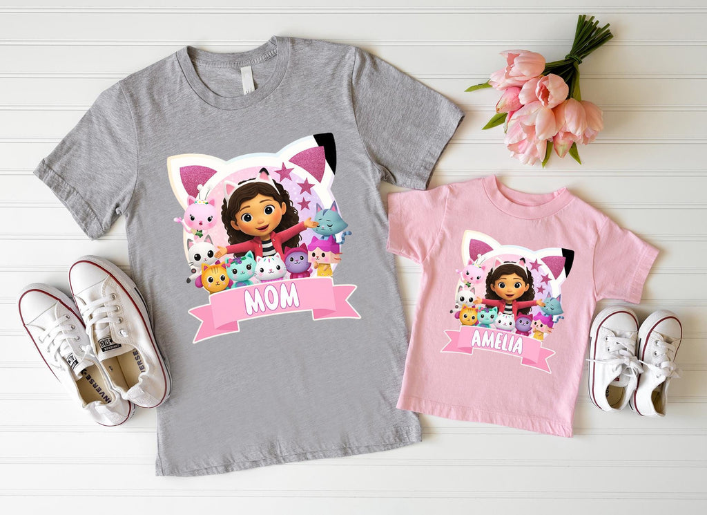 a gray t-shirt with a cartoon character and a pink t-shirt with a similar cartoon character, along with a pair of white sneakers and a bouquet of pink flowers.