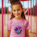 A young girl with brown hair is smiling and wearing a pink t-shirt with a graphic design and text.